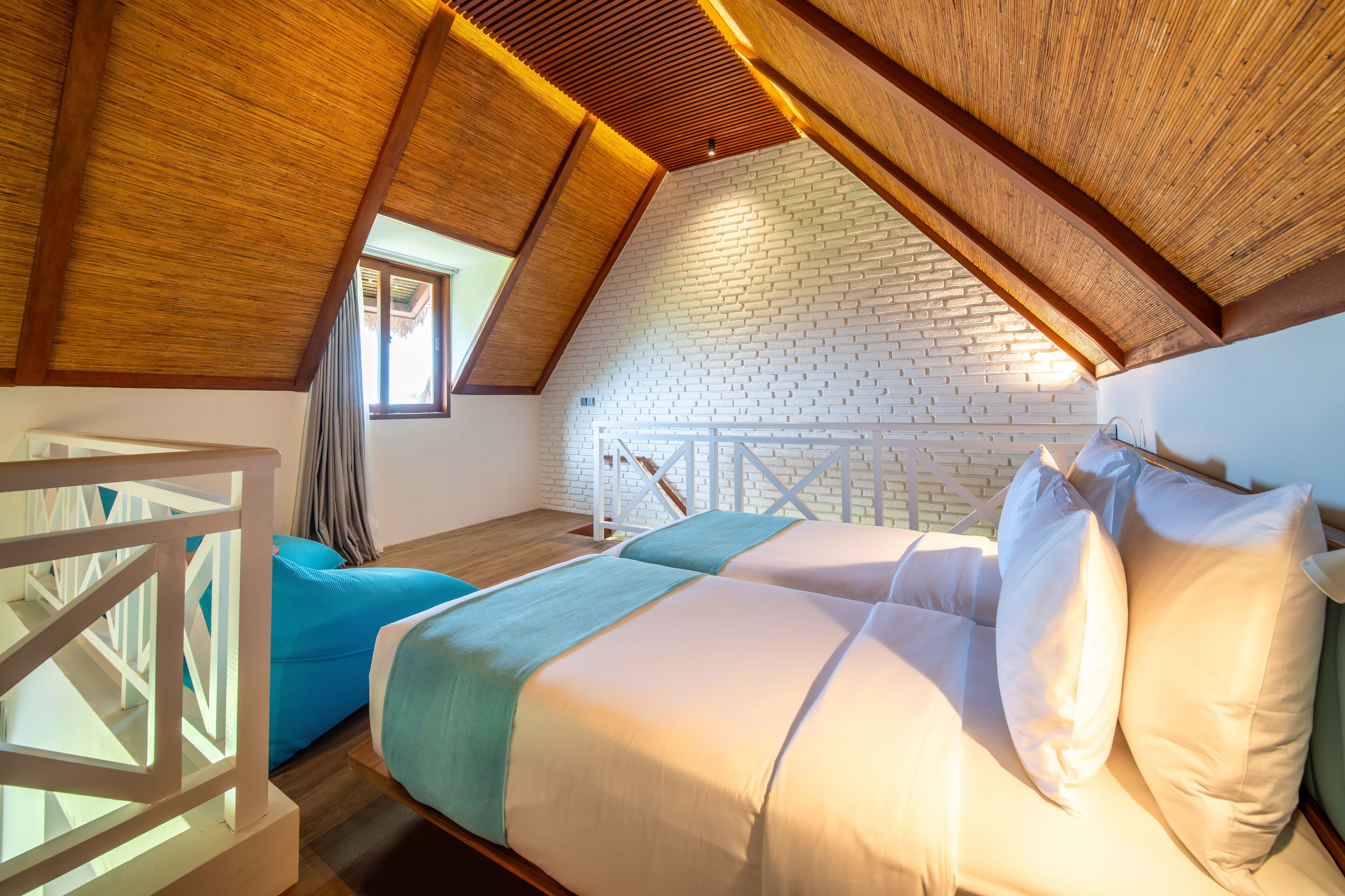 A bedroom with a sloped ceiling, a white brick wall, and a wooden staircase.