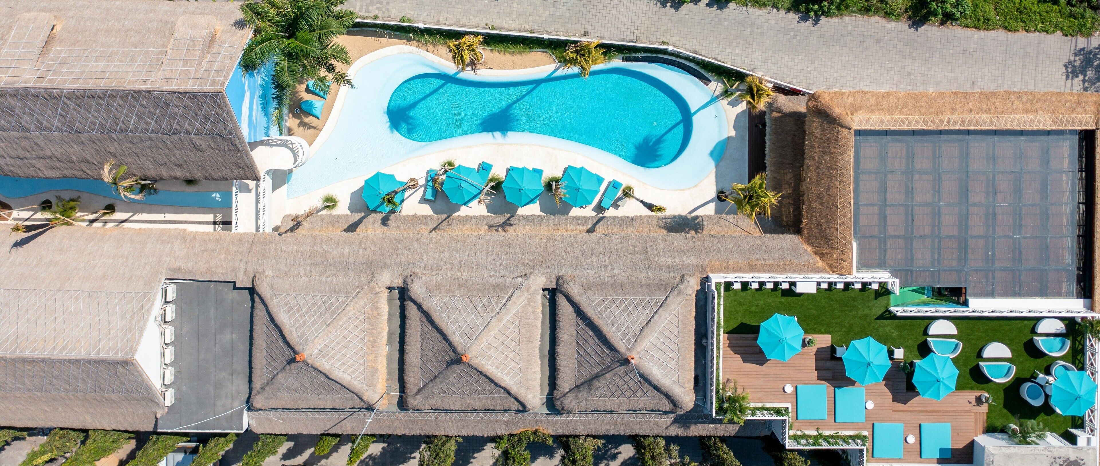 An aerial view of a resort with a swimming pool, sun loungers, and a covered outdoor area.