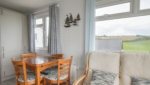 Uma sala de jantar com mesa e cadeiras de madeira, um sofá e vista para o campo pela janela.