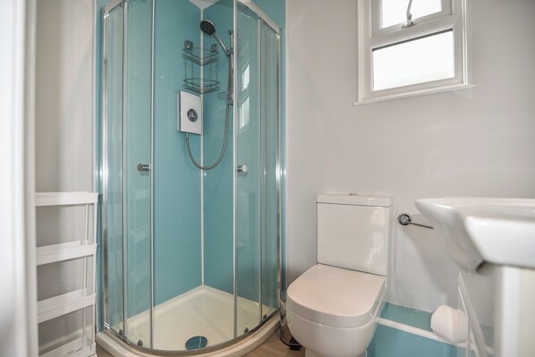 Een badkamer met een douchecabine van glas, een wit toilet en een raam.