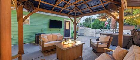 An outdoor patio with a wooden pergola, a fire pit, and seating arrangements.