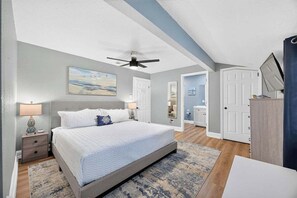 A bedroom with a bed, nightstands, a ceiling fan, and a view of a hallway.