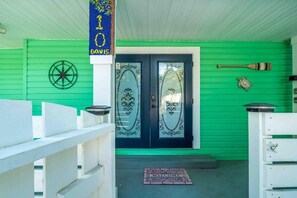 A green building with a white porch, a welcome mat, and a bat and turtle decoration on the wall.