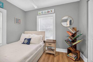 A bedroom with a bed, bedside table, and a wooden bookcase. - Magnolia Cove - Fire Pit, Hot Tub, Downtown (St. Augustine)