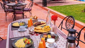 Un área de comedor al aire libre con una mesa dispuesta para el desayuno, incluyendo platos de comida, bebidas y una cafetera.