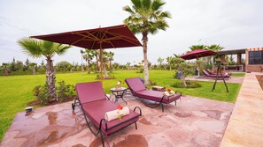 A patio area with two lounge chairs, a table, and a red umbrella. - Igrane House: Ferme D'hôtes (Sidi Abdellah Ghiat)
