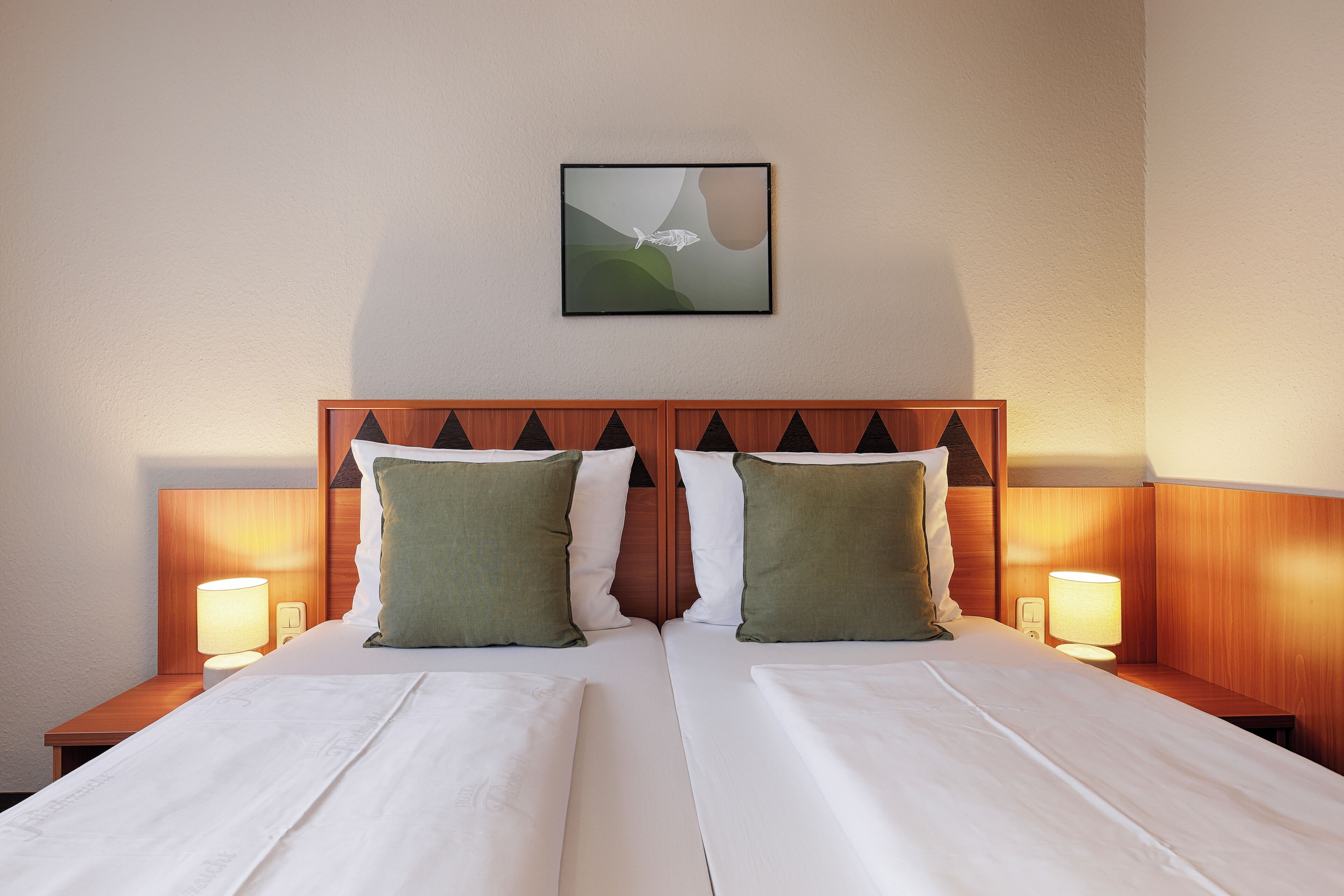 A double bed with two pillows, a wall-mounted artwork, and bedside lamps.