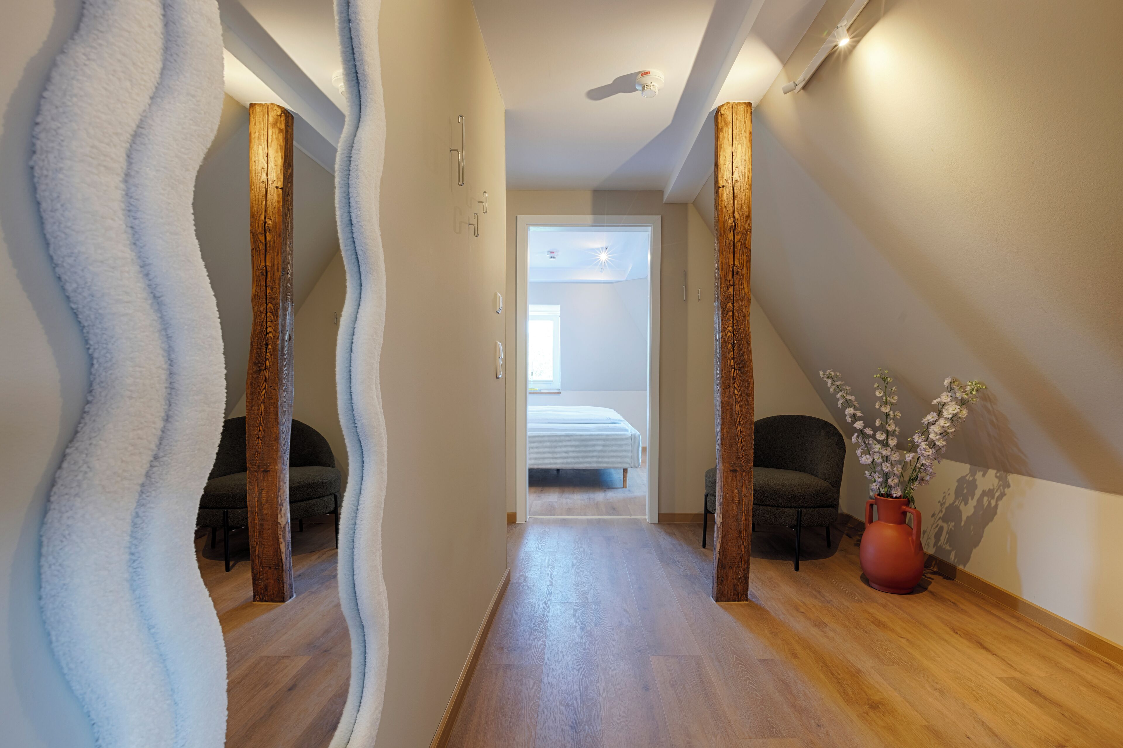 A narrow hallway with wooden flooring and a bed at the end.