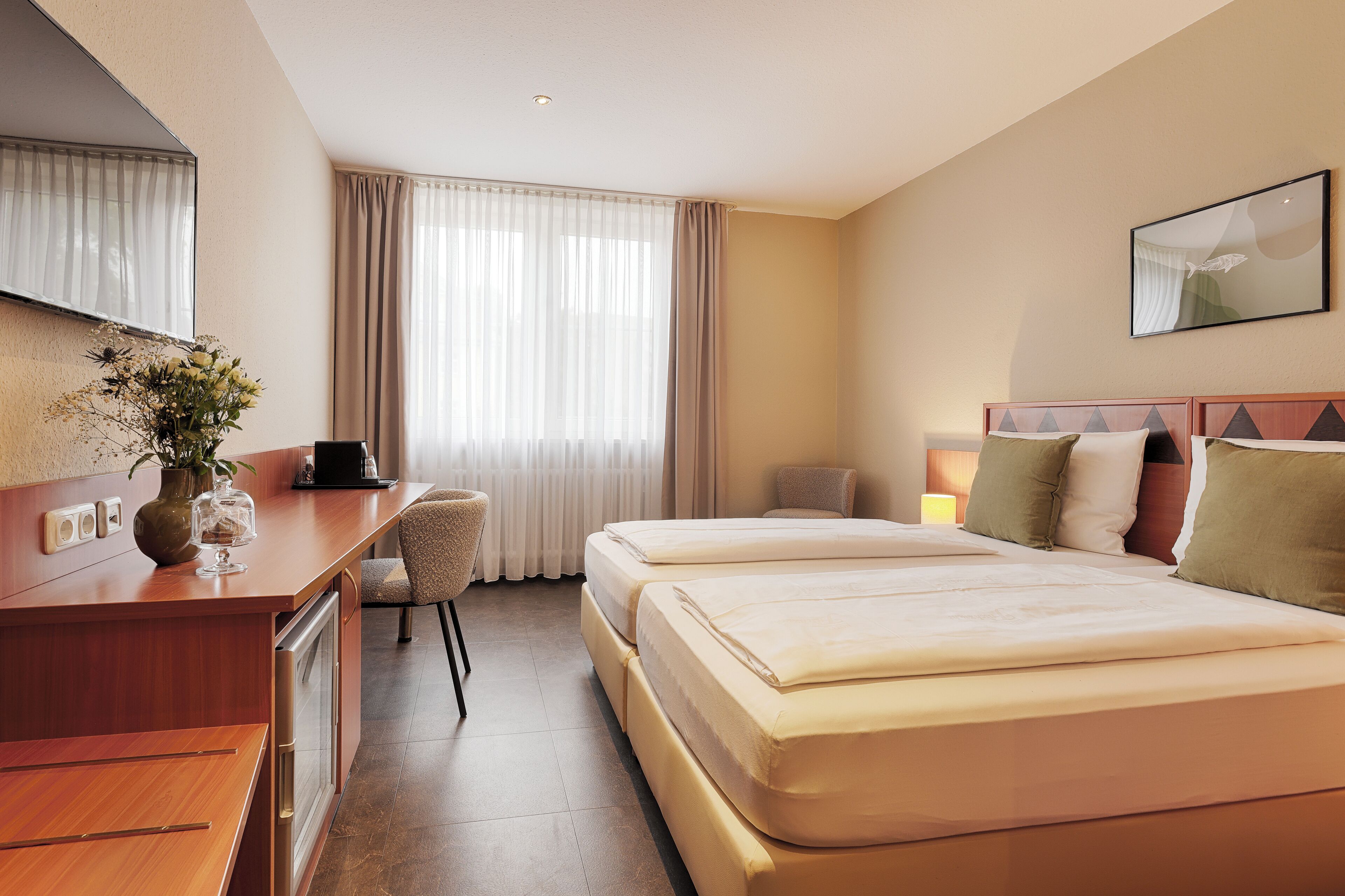 A hotel room with a bed, a desk, a chair, and a window with curtains.
