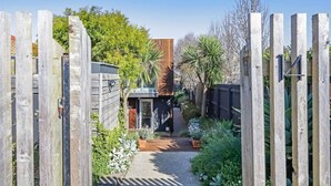 A gated backyard with a pathway leading to a wooden structure, surrounded by various plants and trees. - Silver Ball Retreat (Warrnambool)
