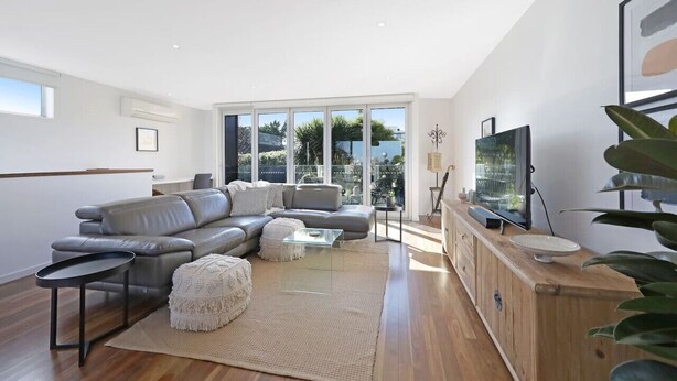 A modern living room with a grey leather sofa, a glass coffee table, and a wooden cabinet with a television. - Silver Ball Retreat (Warrnambool)