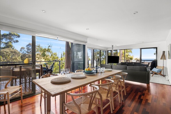 A spacious living area with a large wooden dining table, multiple chairs, a sofa, and a television.