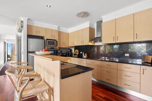 A modern kitchen with wooden cabinets, a central island, and a built-in microwave. - The Eyrie (Lorne)
