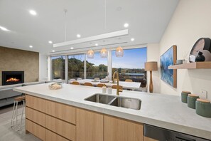 A modern kitchen with a large island, stainless steel sink, and pendant lighting.