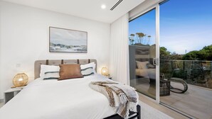 Ein modernes Schlafzimmer mit einem großen Bett, Blick ins Freie durch eine Schiebetür und einem Bild an der Wand.