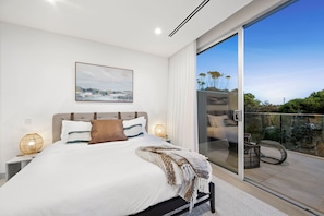 Une chambre moderne avec un grand lit, une vue sur l’extérieur grâce à une porte-fenêtre coulissante et un tableau accroché au mur.