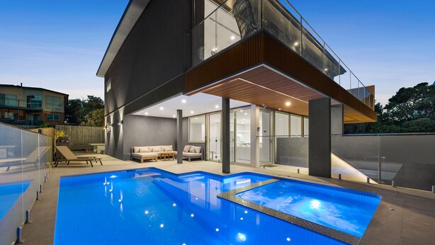 Une maison moderne dotée d’une piscine, d’un patio couvert et offrant une vue sur les environs.