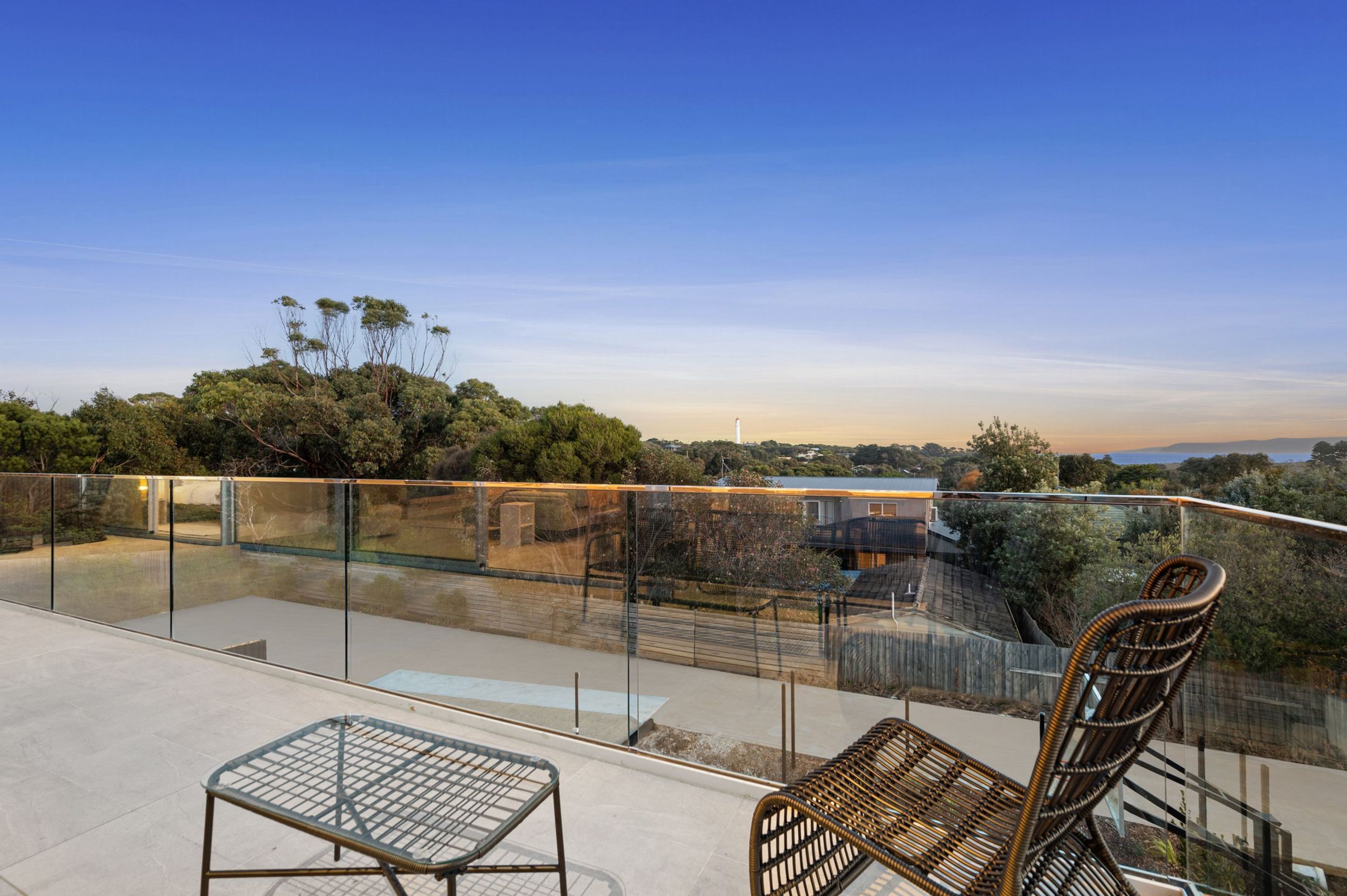 A rooftop terrace with a glass balustrade, two wicker chairs, and a metal table.