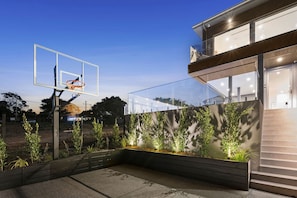 A basketball hoop in a backyard with a modern house in the background.