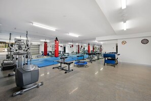 Een sportschool met diverse fitnessapparaten, waaronder loopbanden, krachttoestellen en een tafelvoetbaltafel.