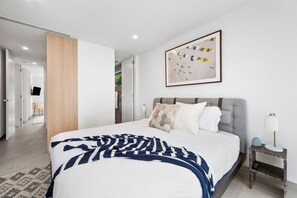 Een moderne slaapkamer met een groot bed, een nachtkastje, een wandlamp en een lijst met een kunstwerk.
