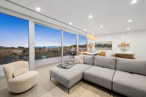 Un salon moderne doté d’un grand canapé d’angle, d’un fauteuil rond et d’un coin repas offrant une vue sur le paysage.