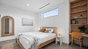 Ein modernes Schlafzimmer mit einem hölzernen Bett, einem Nachttisch mit Lampe, einem Bücherregal und einem großen Spiegel.