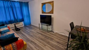 Kompakti olohuone, jossa on sohva, televisio, pieni pöytä ja huonekasvi.
