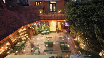 Un patio al aire libre con mesas y sillas verdes, luces colgantes y plantas en macetas.