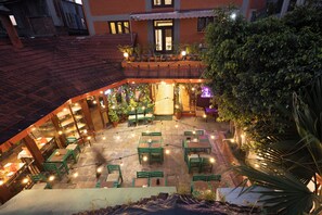 Un patio al aire libre con mesas y sillas verdes, luces colgantes y plantas en macetas.