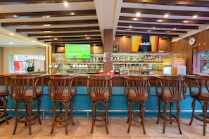 A bar area with wooden chairs, a counter with a variety of bottles, and a television screen displaying a sports game. - Aawas Boutique Hotel - Central Thamel (Kathmandu)