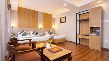 A hotel room with two beds, a wooden desk, a chair, a small table, a bedside table, and a wardrobe.
