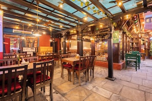 An indoor restaurant with wooden tables and chairs, a brick wall, and a glass ceiling. - Aawas Boutique Hotel - Central Thamel (Kathmandu)