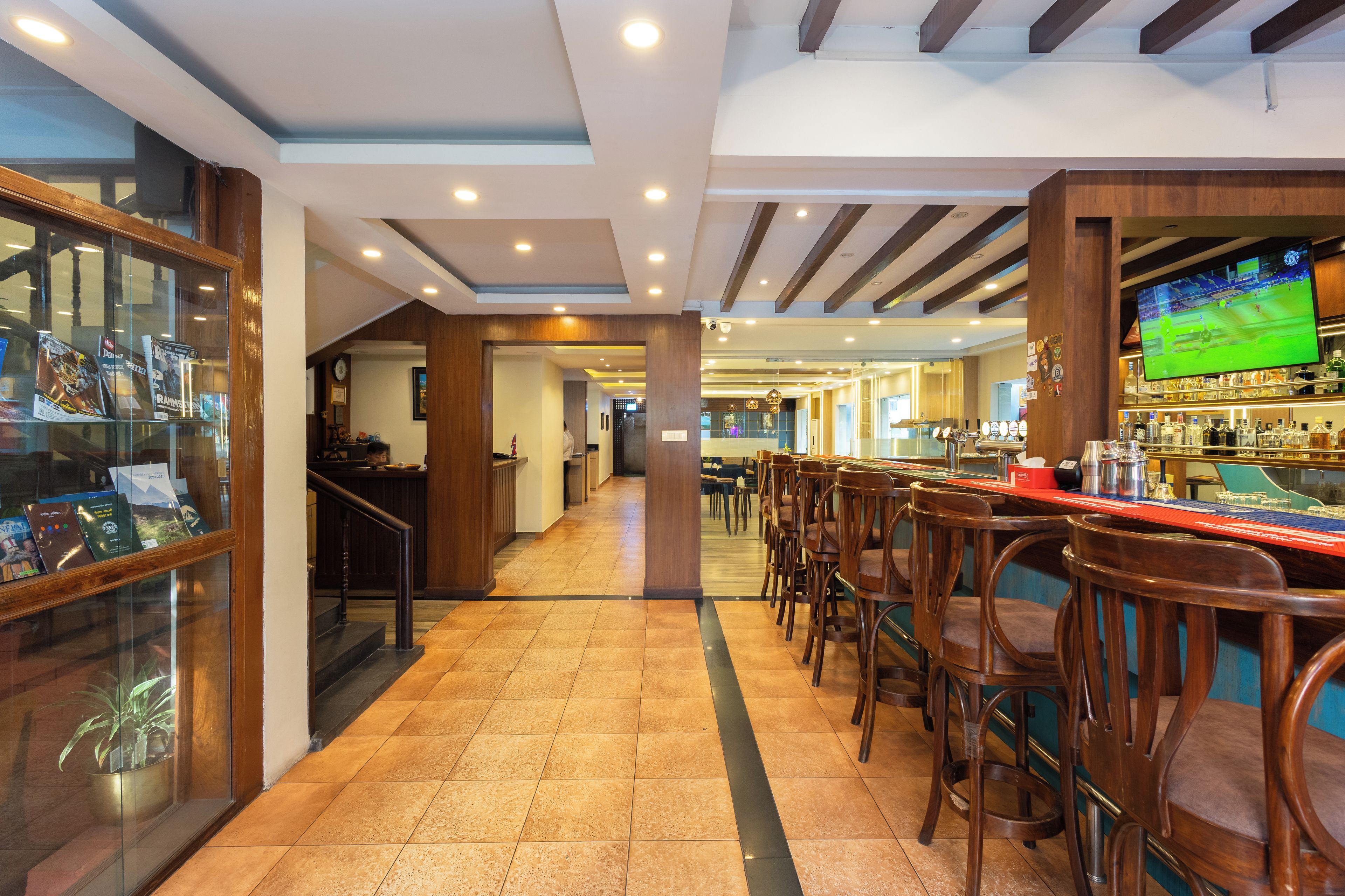 Zona de bar con sillas de madera y una pantalla de televisión mostrando un evento deportivo.
