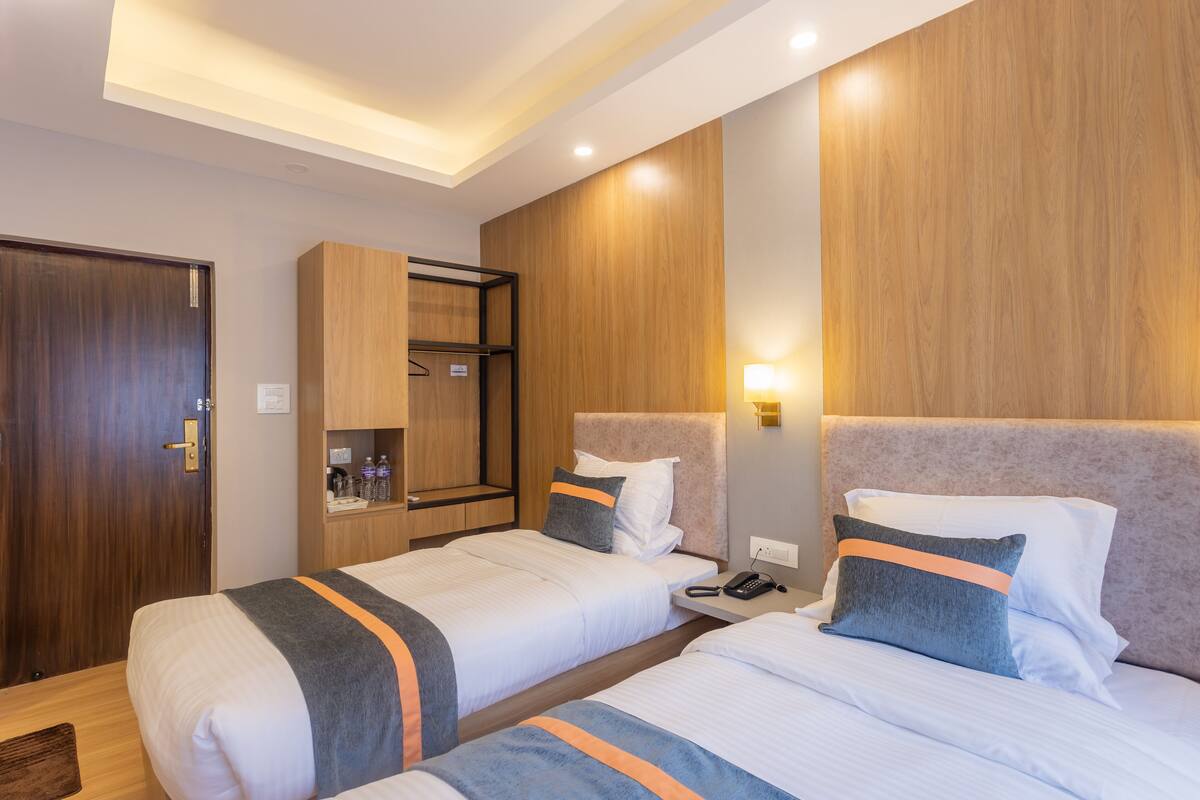Une chambre d’hôtel avec deux lits, des lambris en bois aux murs, une armoire et une table de chevet avec un téléphone et une bouteille.