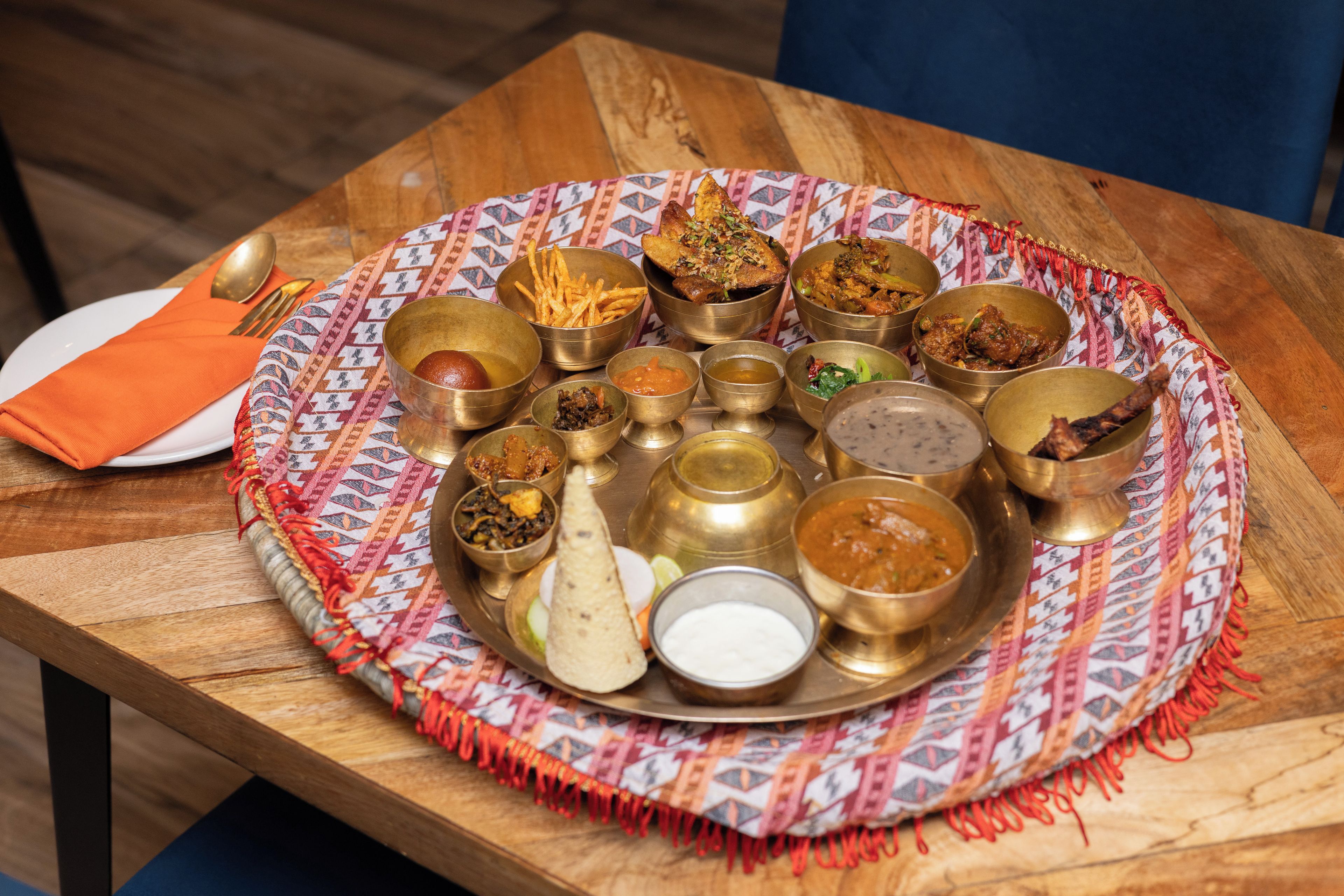 Una comida tradicional india con varios platos y utensilios sobre una mesa de madera.