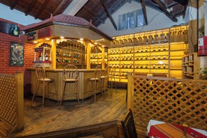 Zona de bar con estantes de madera llenos de botellas, barra y asientos.