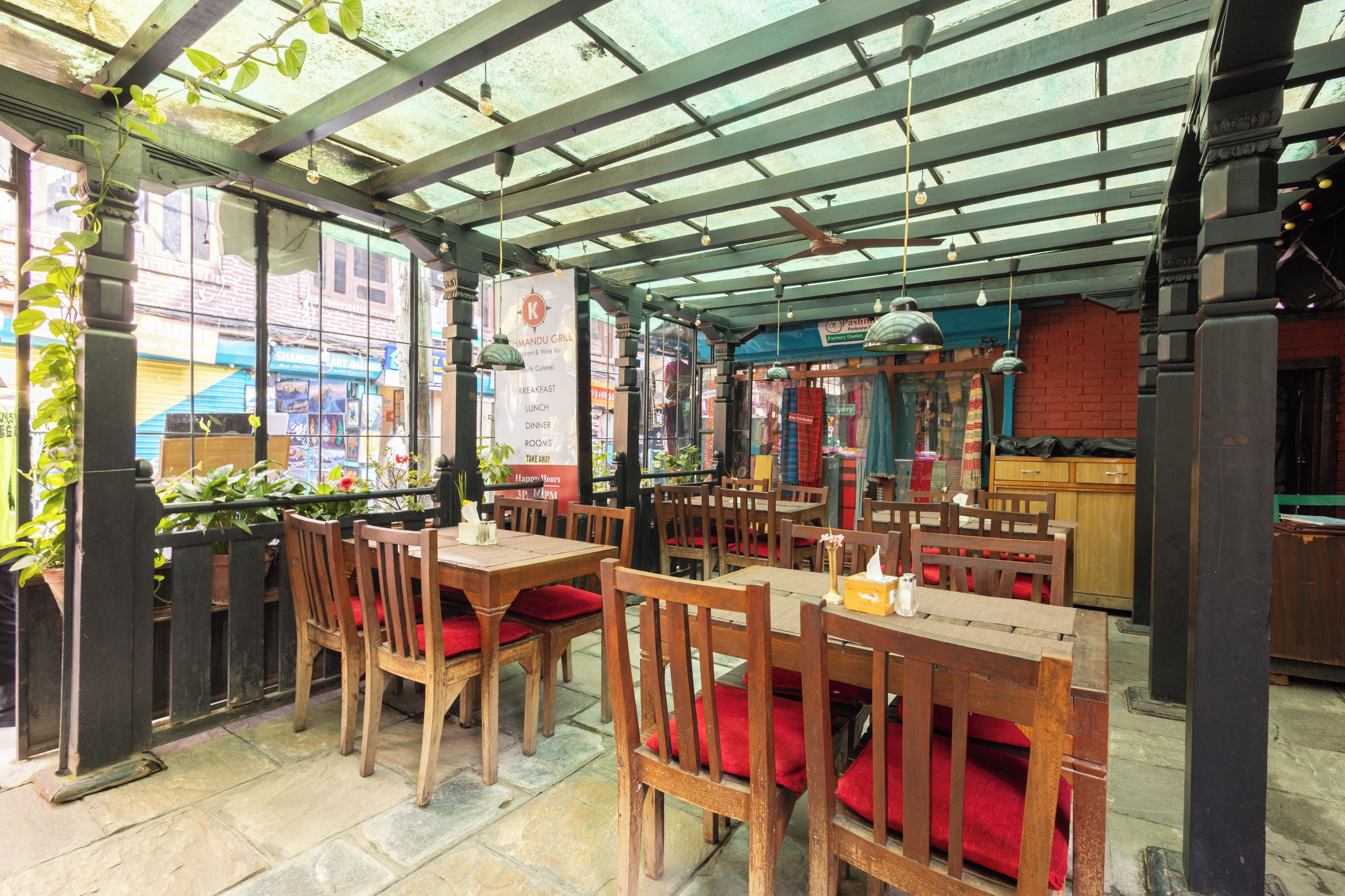An indoor dining area with wooden tables and chairs, a glass ceiling, and a view of the street outside.