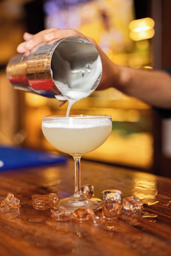 A person pouring a liquid into a glass with a stemmed base, with ice cubes on the surface. - Aawas Boutique Hotel - Central Thamel (Kathmandu)