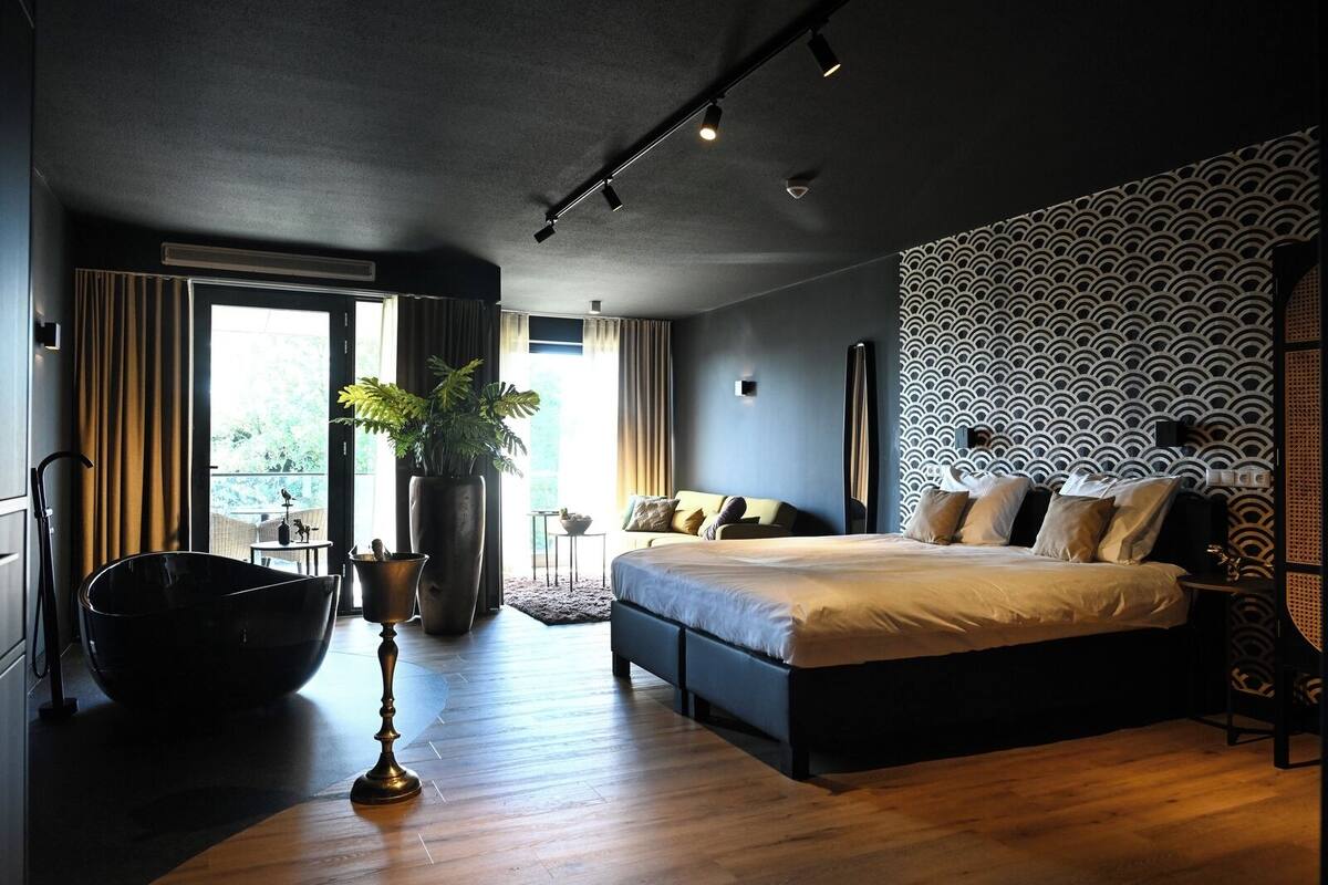 A modern bedroom with a large bed, a potted plant, and a view of the outdoors.