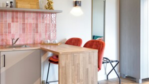 A modern kitchen with a wooden island, a sink, and a countertop with a kettle. There is a chair with a red cushion and a mirror on the wall. - Wapen van Hengelo Residence Suites - LOGIES ONLY - digital key by APP and email (Hengelo)