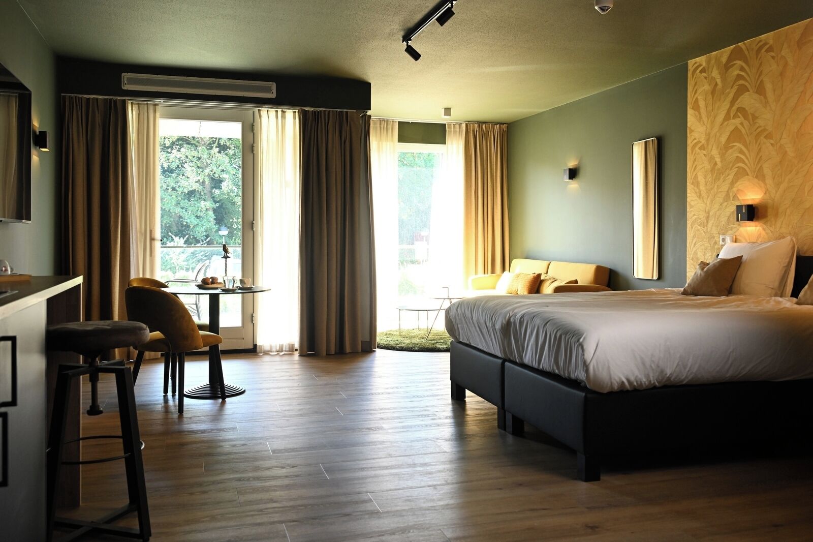 Ett modernt hotellrum med en stor säng, ett skrivbord med en stol och utsikt över grönområden utanför.