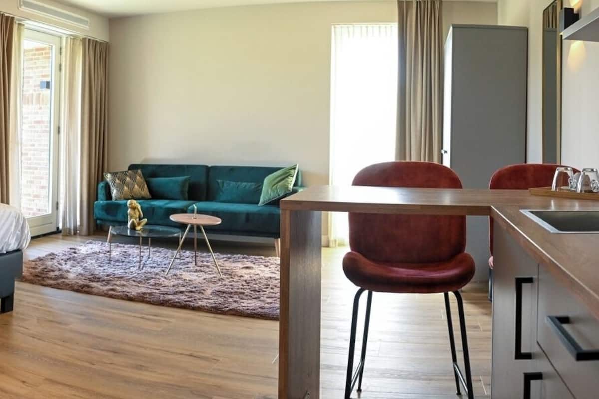 A bedroom with a bed, a small table, a sofa, and a kitchenette area.