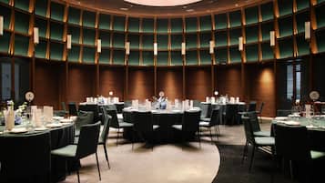 Een congreszaal met meerdere ronde tafels, elk voorzien van stoelen, glazen en decoratieve middelpunt.