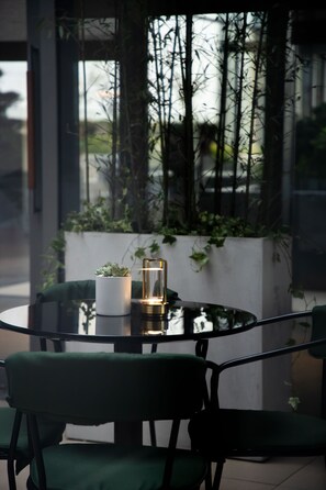A round glass table with a potted plant and a lantern, surrounded by green chairs, in a modern indoor setting with large windows and greenery. - Artyzen NEW BUND 31 Shanghai (Shanghai)