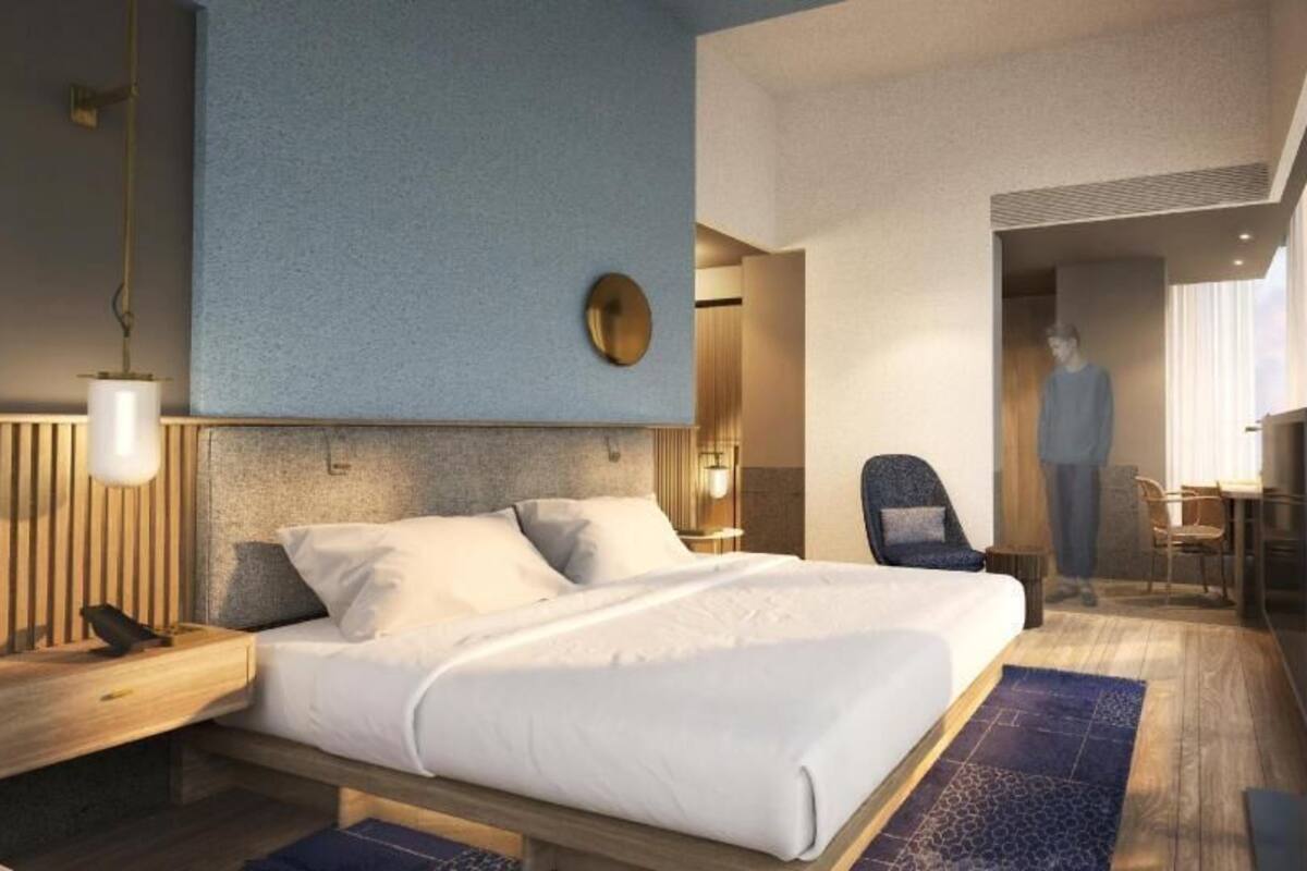 A modern hotel room with a large bed, bedside tables, a chair, and a desk.