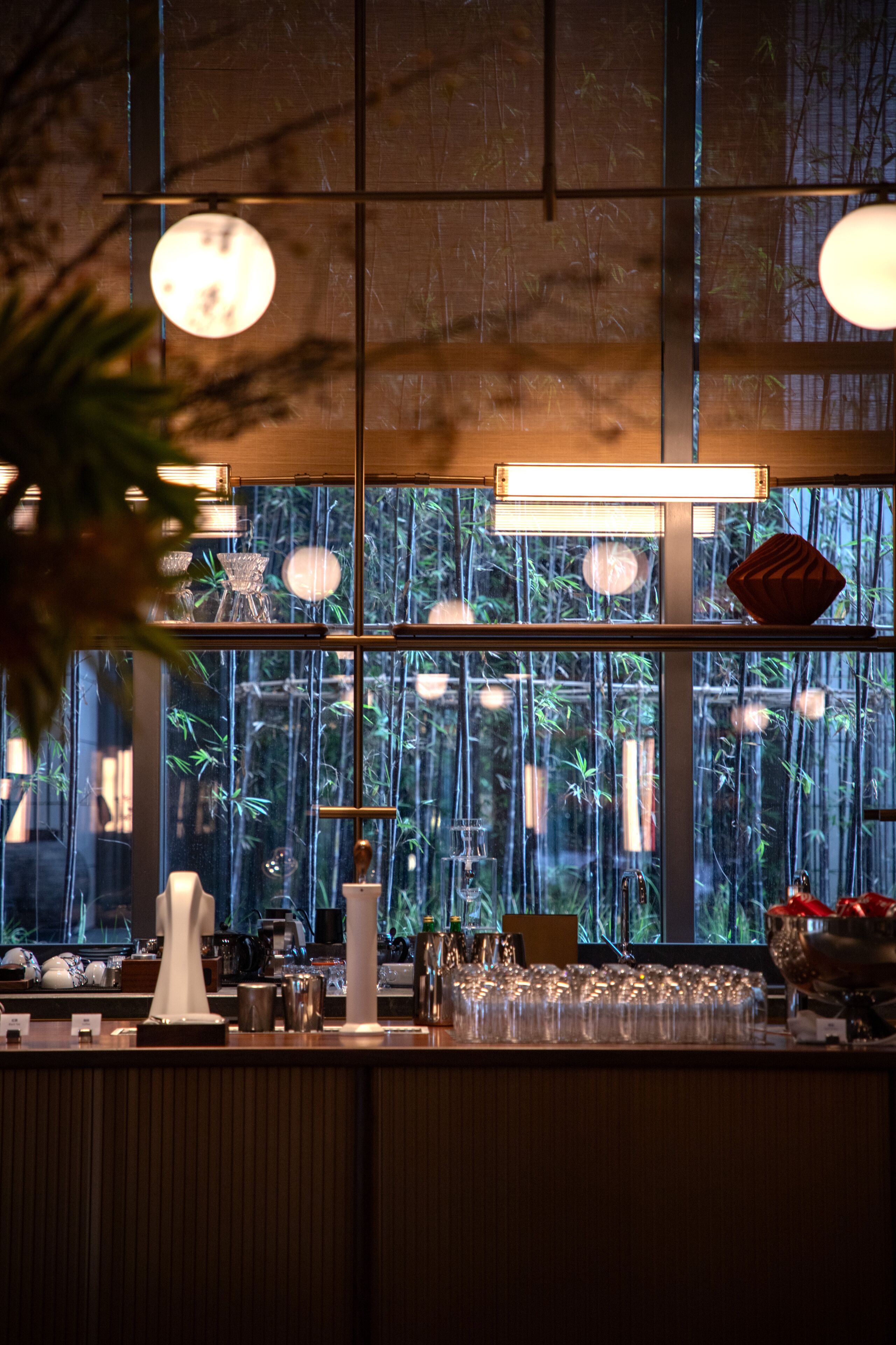 Eine Bar mit großem Fenster, Regalen für Gläser und hängenden Lampen.