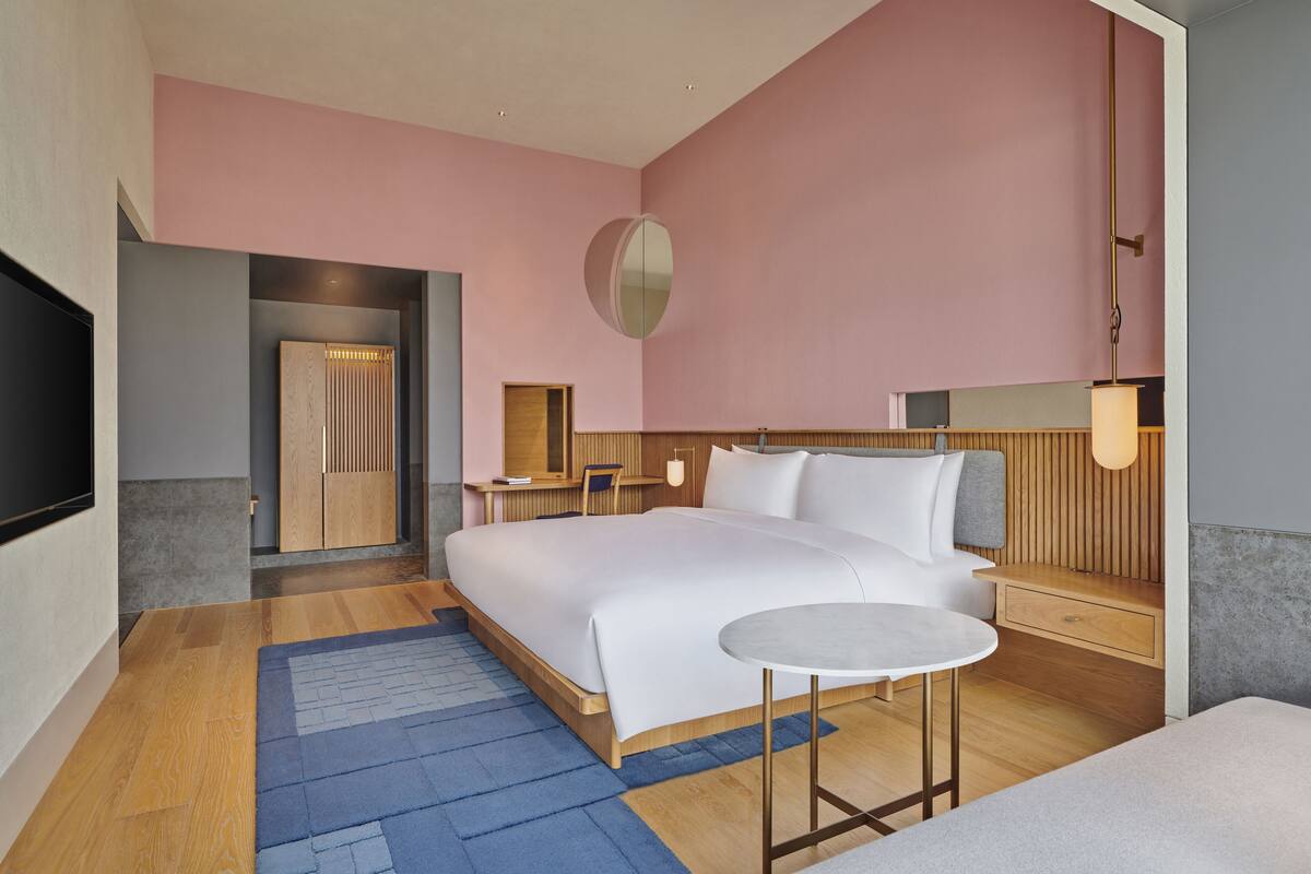 A modern hotel room with a large bed, bedside tables, a round table, and a TV mounted on the wall.
