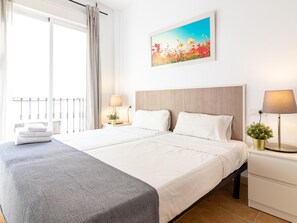 A hotel room with a bed, two bedside tables, a nightstand, a window with curtains, a balcony, and a painting on the wall. - Bright 1BR Apartment with AC, Modern Amenities, and WIFI in Málaga (Málaga)