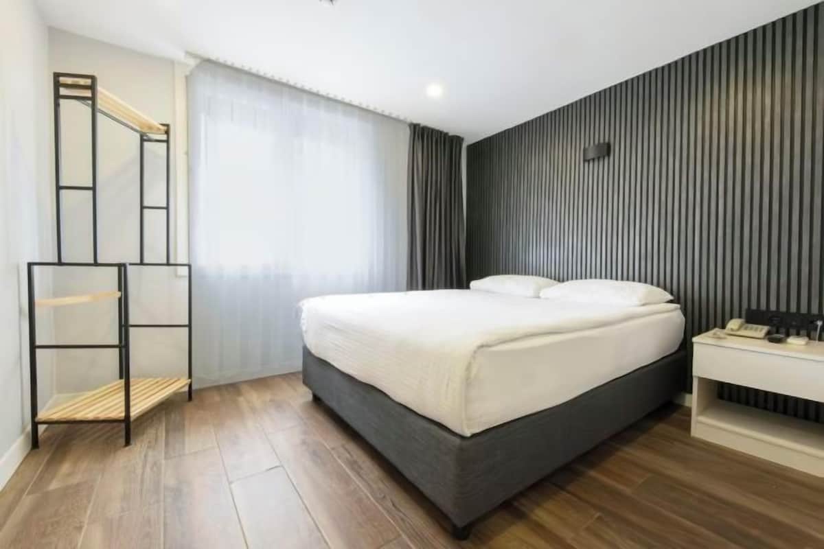 A modern bedroom with a bed, a bedside table, a mirror, and a wooden floor.
